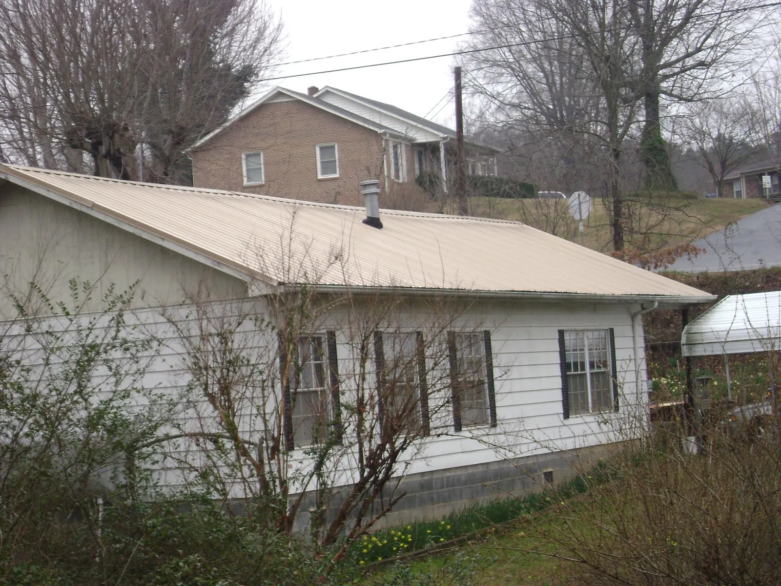 Tan metal roof on a white sided house set into a hillside — Commercial Roofing by Roofing Brothers in Blue Ridge